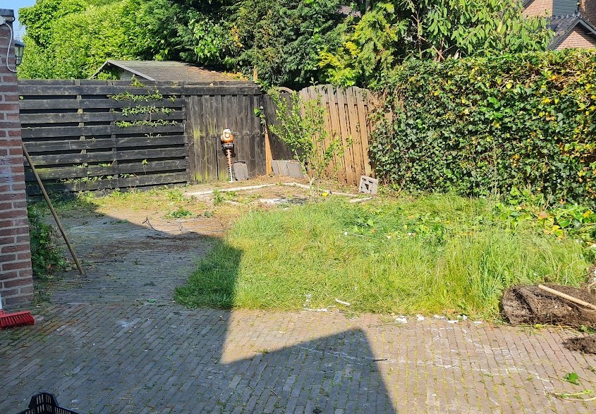 De tuin vóór de aanleg: verwilderd gras, oude klinkers en een houten schutting