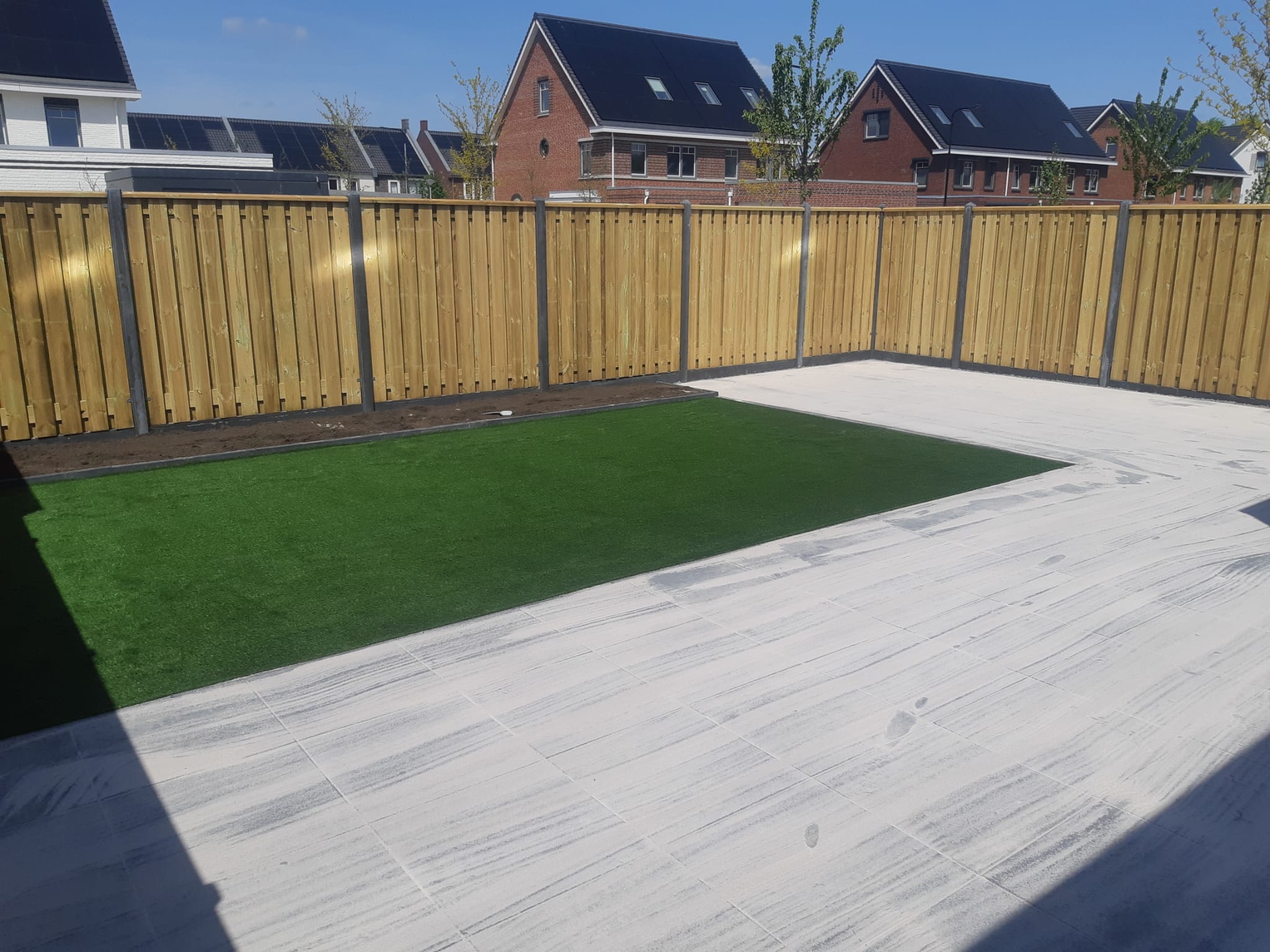 Kunstgras naast een terras in houtlook tegels, omringd door een nieuwe houten schutting